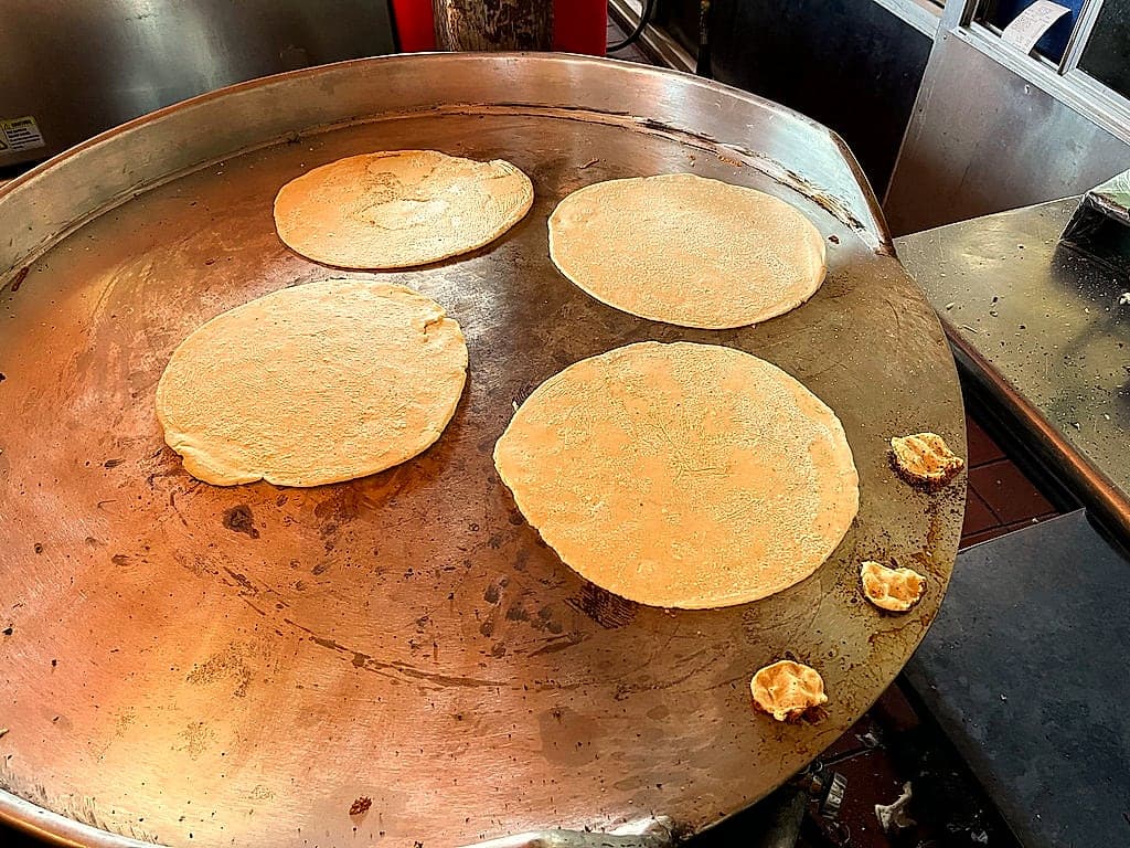 Tortillas cooking on a steel comal.
